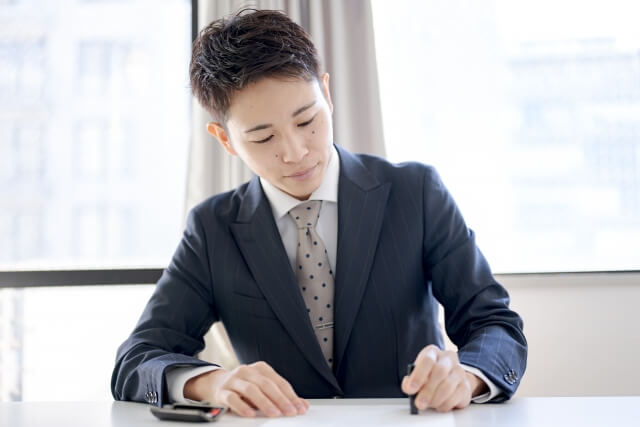 デスクで書類を書くスーツの男性